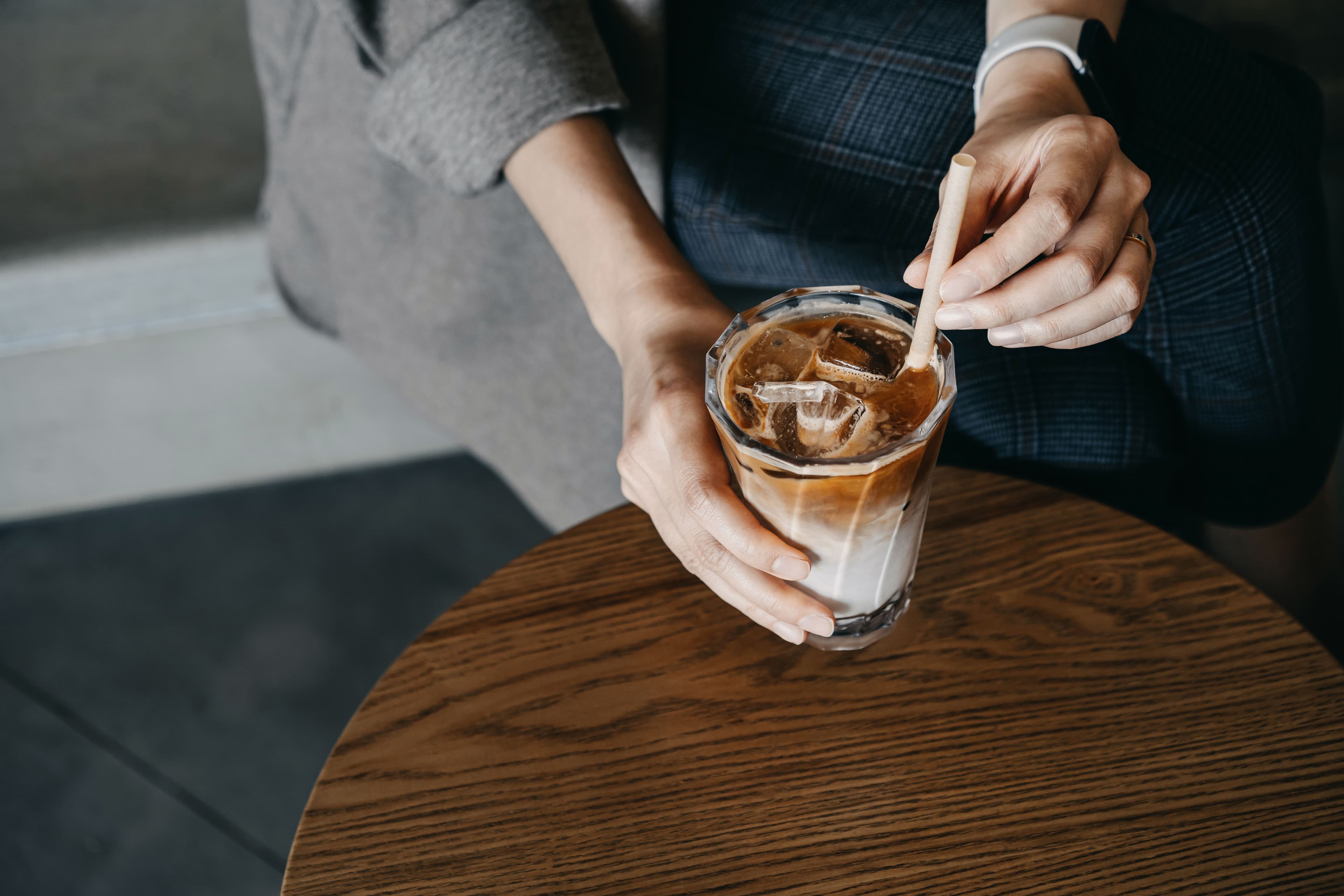 A person holds a glass of iced coffee with a straw. 